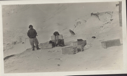 Image of Inuit man with dog whip by many crates. Note walrus head and mittens