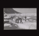 Image of Inuit and crewmen look at typewriter(?) on ice pan. One holds long pole  [b&w]