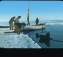 Image of Small sail boat by shore; three men, Inuit boy on stomach, woman ....