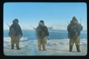 Image of Three men watching iceberg. Each has coil of line on his back