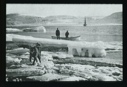 Image of Iceberg remains. Two men with dory by one. Dog on ice in foreground