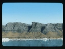 Image of Large sand piles against striated cliffs. Ice floes at edge