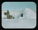 Image of Inuit man with pipe outside snow igloo.Equipment near