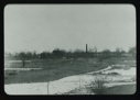 Image of Wintry landscape with orchard. Buildings and smoke stack beyond       