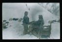 Image of Man on sledge having his foot warmed by another. Dogs resting near [Minik warming Ekblaw's foot]