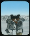 Image of Two inuit women, foreheads together, lighting cigarettes