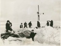 Image of Six men by windsock pole. Two others shovel snow off their tent. Soviet Polar Expedition