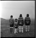 Image of Three Inuit women and a girl in traditional dres, rear view