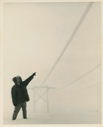 Image of Man pointing to wires running from low support, during snow storm. Thule AFB