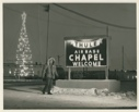Image of Man near Base Chapel sign. Christmas "tree" lights near. Thule AFB