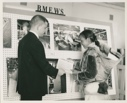Image of RCA employee presents papers to Inughuit woman by BMEWS display board [Aqattaq Qujakitsoq and baby Atangana]