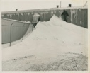 Image of Man standing on snow pile near long building at Thule AFB