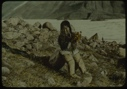 Image of Eskimo [Inuk] girl sitting on rock holding flowers