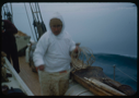 Image of Eskimo [Inuk] man w/ glasses, holding coiled line, by kayak on deck
