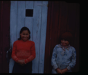 Image of Two Eskimo [Inuit] girls by wooden building