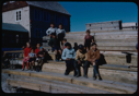 Image of Group of Eskimos [Inuit] sitting on stacked lumber