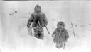 Image of Inuit father with saw and a child, in snow wearing furs